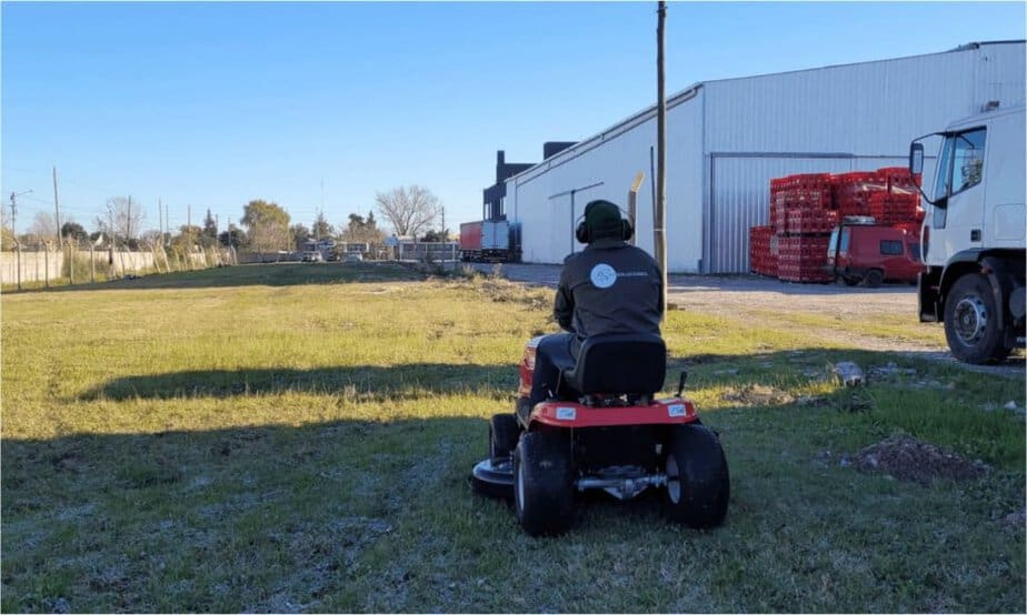 Operario de EV Soluciones cortando césped con tractor parquero en un predio industrial